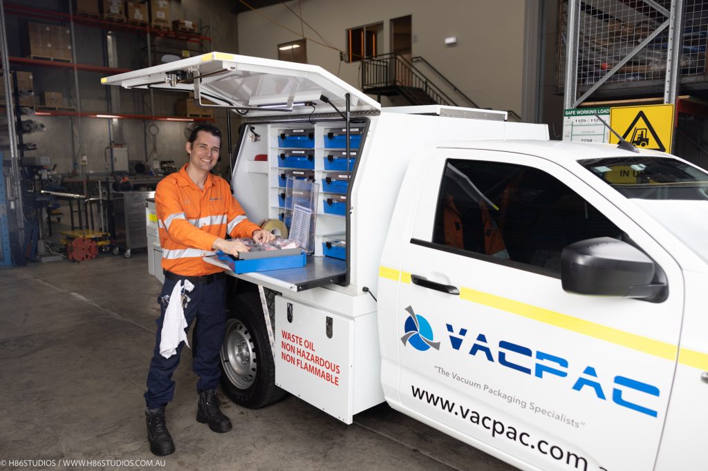 A VACPAC technician standing at the back of his truck prepping parts for a vacuum packaging machine service.